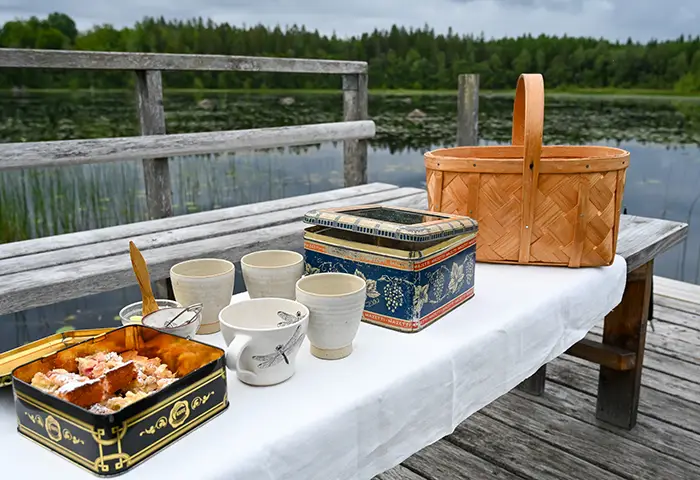 Kakor i burkar, kaffekoppar och en picknick-korg uppdukat bredvid en sjö en sommarkväll.