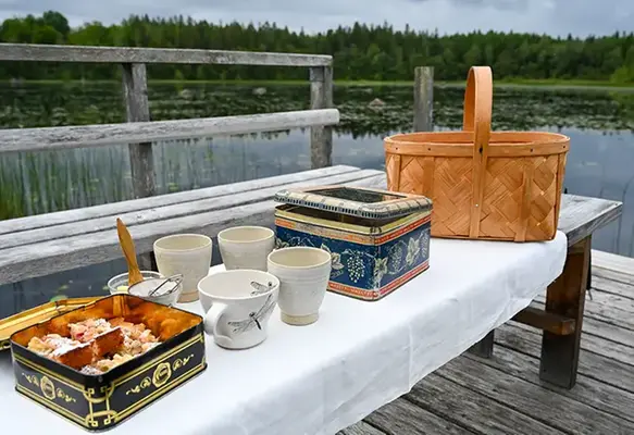 Kakor i burkar, kaffekoppar och en picknick-korg uppdukat bredvid en sjö en sommarkväll.